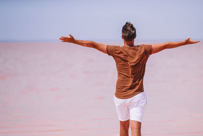 Rear view of man standing at beach against sky