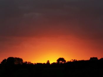 Silhouette trees on field against romantic sky at sunset