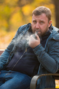 Portrait of mature man smoking while sitting on bench at park