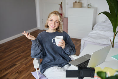 Young woman using mobile phone while sitting on bed at home