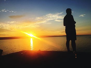 Silhouette man standing on beach against sky during sunset