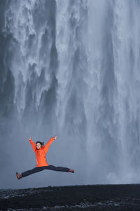 Woman jumping in front of skógafoss waterfall in south iceland
