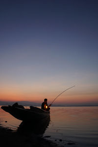Silhouette fishing rod on sea against sky during sunset