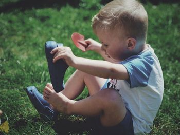 Side view of boy wearing shoes while sitting on grassy field
