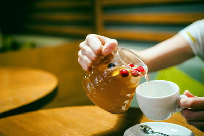 Cropped image of woman pouring drink in coffee cup at restaurant