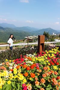 Woman standing by flowering plants against sky