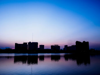 Silhouette buildings by lake against sky at sunset