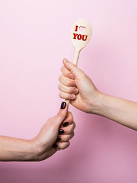 Cropped hands of women holding text on wooden spoon against wall