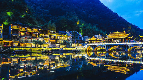 Illuminated bridge over river against buildings