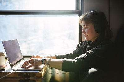 Businesswoman using laptop while sitting by window in train