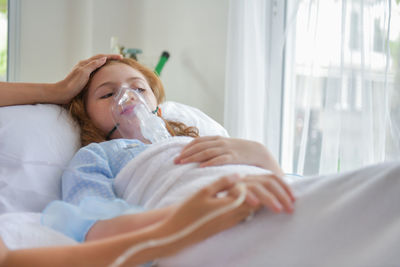 Cropped image of woman touching girl lying on bed in hospital ward