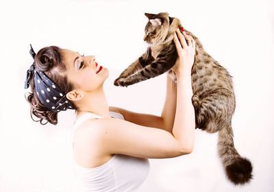 Young woman carrying cat against white background
