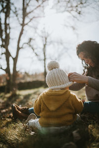 Mother and daughter wearing warm clothing while sitting on land