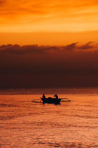 Silhouette people on boat in sea against orange sky