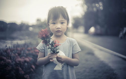 Portrait of innocent girl holding flowers at roadside