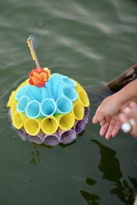 Cropped hand of woman reaching for religious offering floating on river