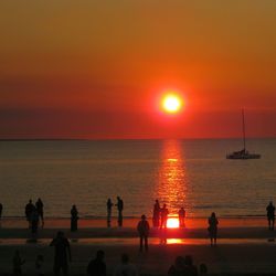 People enjoying at beach against sky during sunset