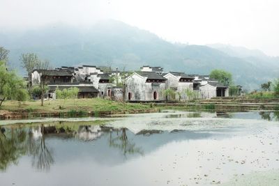 Houses by lake and buildings against sky