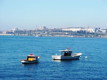 Boats sailing in sea against clear blue sky