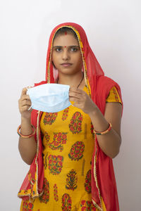 Portrait of woman holding flu mask standing against white background