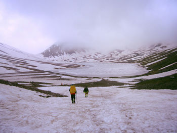 Rear view of people walking on snow covered mountain