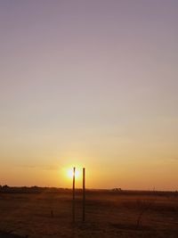 Silhouette wooden posts on field against sky during sunset