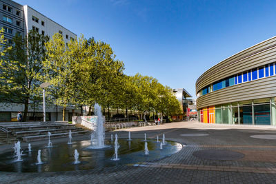 Street amidst trees and buildings against clear blue sky