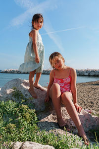 Side view of two sisters sitting on rock at beach