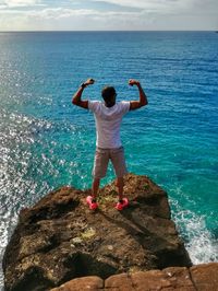 Rear view of man standing on rock by sea