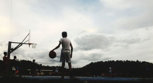 Group of people practicing basketball against sky