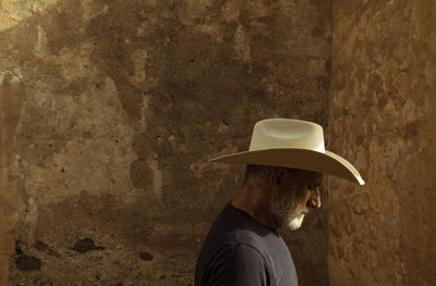 Side view of adult man in cowboy hat against wall