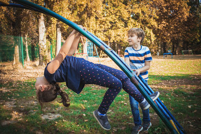 Boy standing by sister playing on jungle gym at park