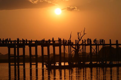 Silhouette people by pier on sea against sky during sunset