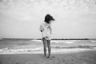 Rear view of woman standing on shore at beach against sky