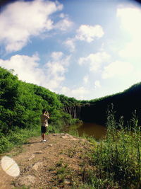 Rear view of man photographing while standing on field against lake