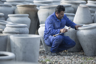 Man with clipboard looking at clay jug production at industrial pot factory