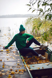 A woman in a green sweater sits in an old wooden boat on a lake in autumn in the village