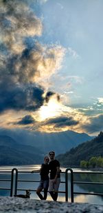 Friends on railing against sky during sunset