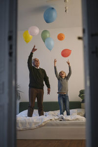 Happy grandfather and grandson playing with balloons on bed at home