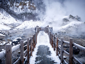 Scenic view of snow covered footbridge leading towards hot spring