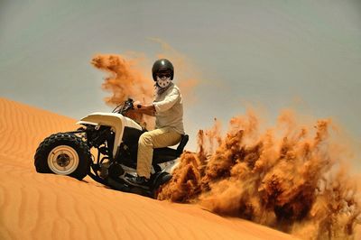 Man riding quadbike on sand against sky