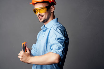 Man holding mobile phone while standing against gray background