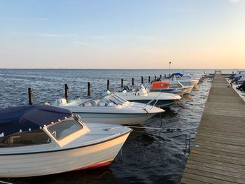 Boats moored in sea against sky during sunset