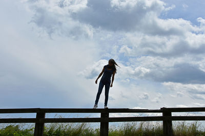 Full length of woman standing on railing against cloudy sky