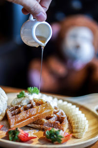 Close-up of person pouring honey on waffle