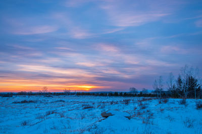 Scenic view of snow covered field against sky at sunset