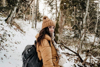 Woman wearing hat in forest during winter. backpack, hiking, snow.