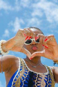 Portrain of a young adult showing love sign at the beach against sky