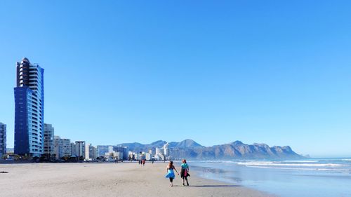 People walking on beach against clear sky