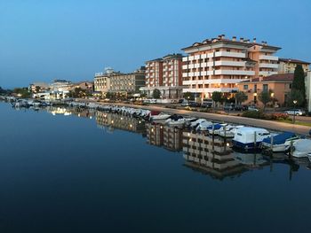 Reflection of buildings in lake against clear blue sky